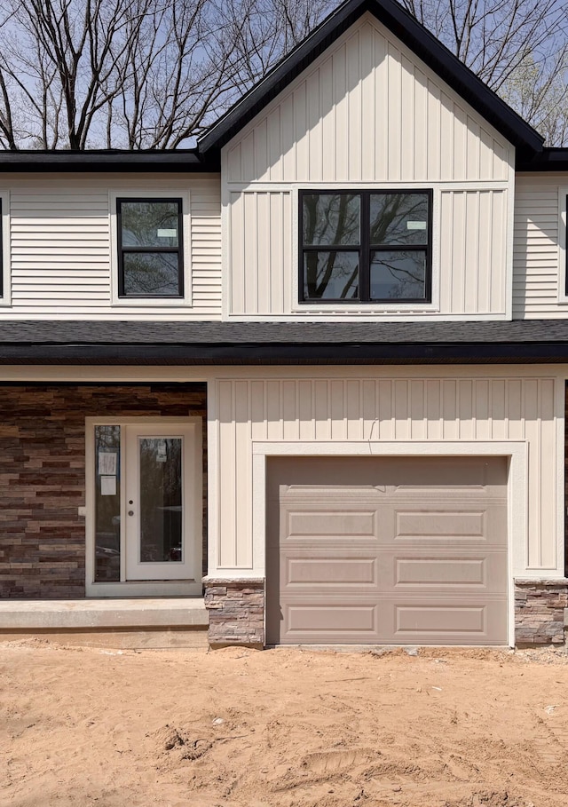 view of front facade featuring stone siding, board and batten siding, dirt driveway, and an attached garage