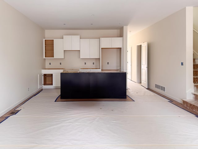 kitchen with a kitchen island, baseboards, visible vents, and white cabinets