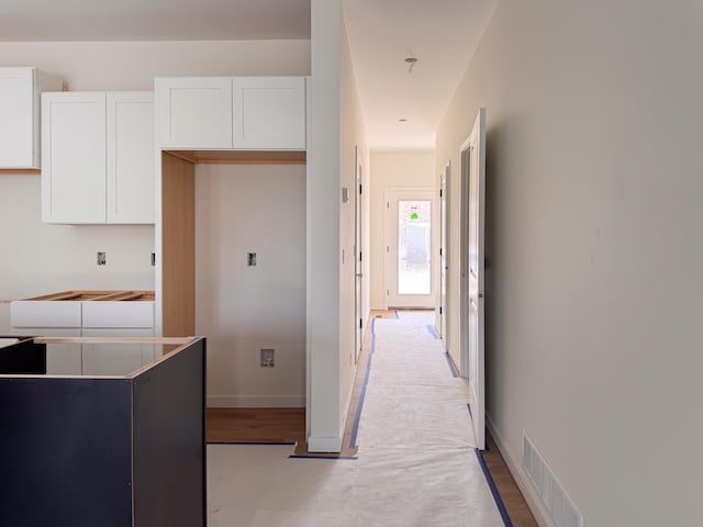 corridor with baseboards, visible vents, and wood finished floors