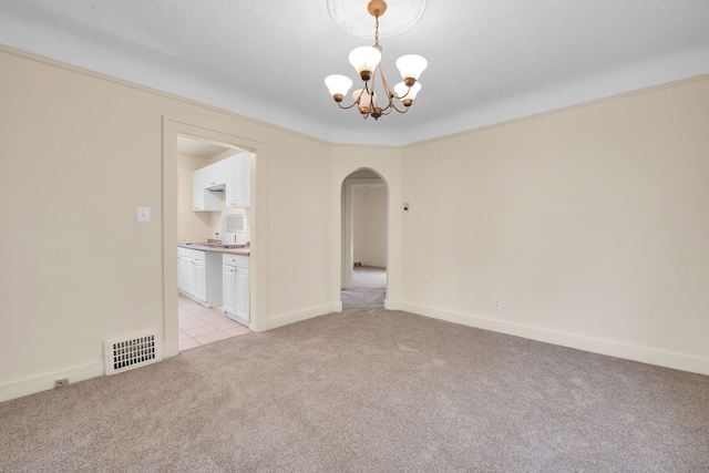 spare room with light colored carpet, crown molding, and an inviting chandelier