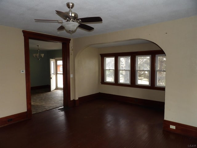 empty room featuring ceiling fan with notable chandelier and dark hardwood / wood-style flooring