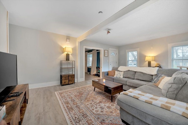 living room featuring beamed ceiling, light hardwood / wood-style flooring, and a wealth of natural light