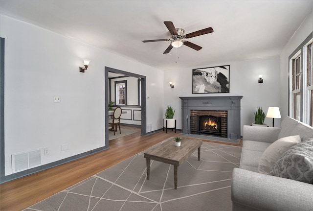 living room featuring wood-type flooring, a brick fireplace, and ceiling fan