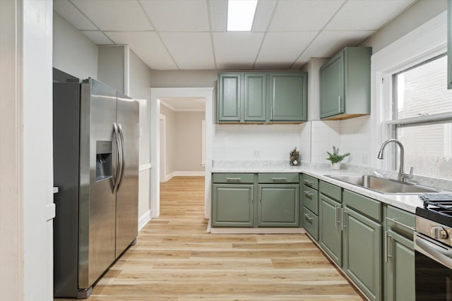 kitchen with sink, stainless steel appliances, green cabinets, backsplash, and light wood-type flooring