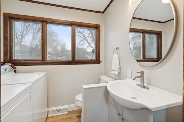 bathroom with washing machine and clothes dryer, wood-type flooring, toilet, vanity, and ornamental molding