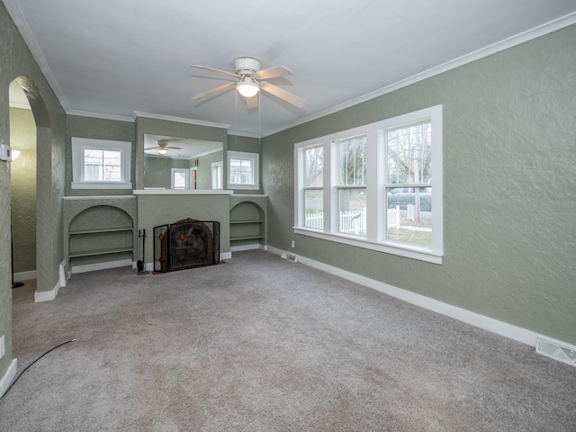 unfurnished living room featuring ceiling fan, plenty of natural light, carpet floors, and ornamental molding