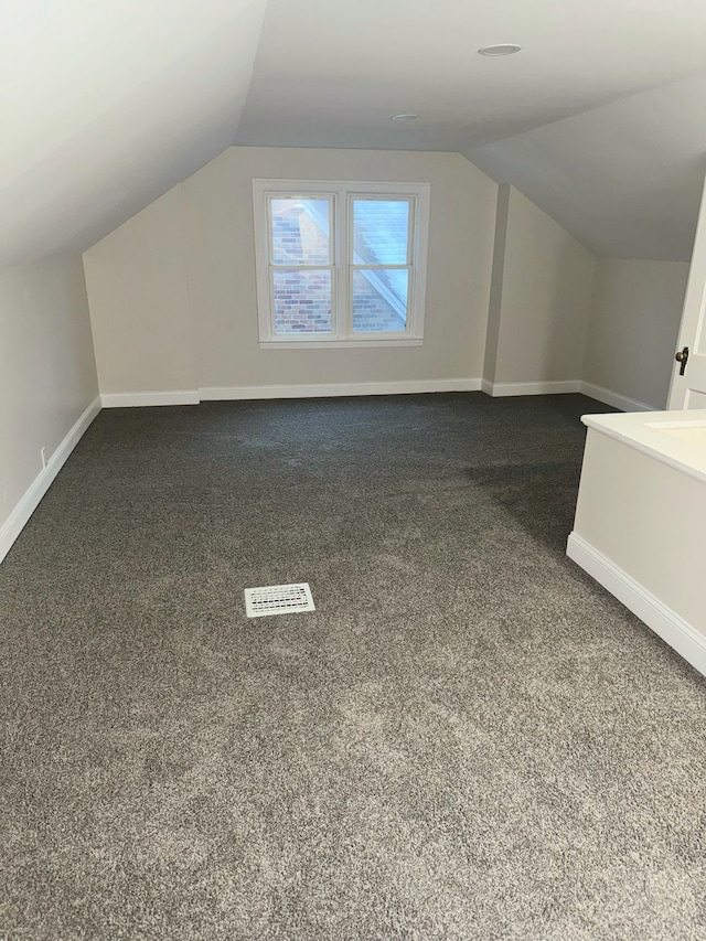 bonus room with dark carpet and vaulted ceiling