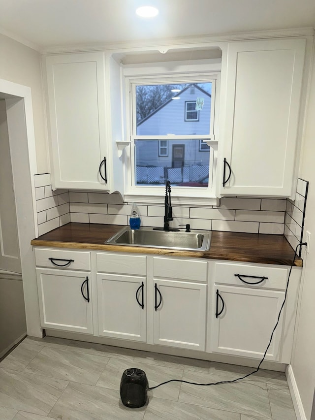 kitchen with decorative backsplash, white cabinetry, sink, and wooden counters