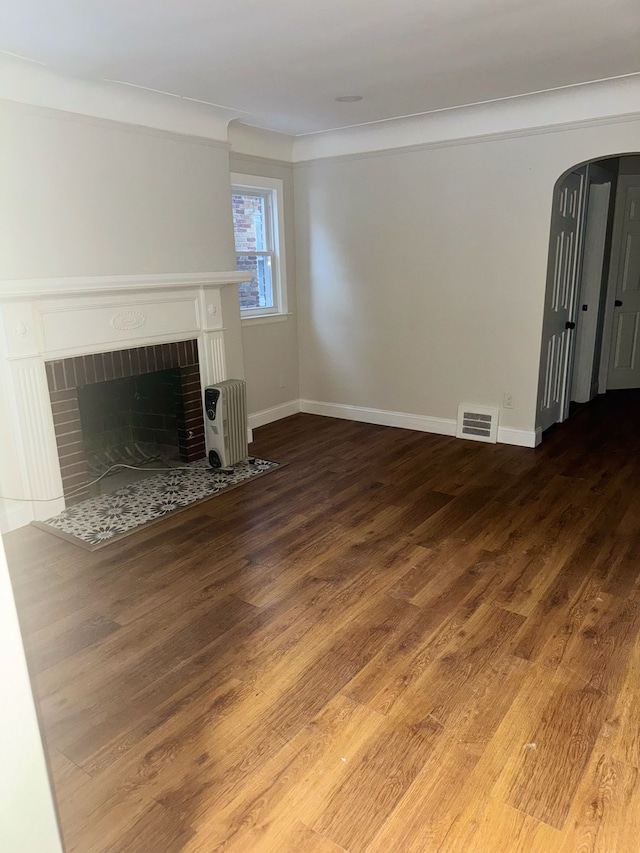 unfurnished living room featuring wood-type flooring, a brick fireplace, and crown molding