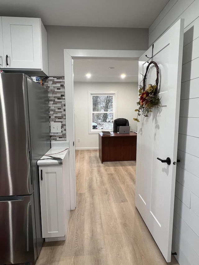 kitchen with tasteful backsplash, stainless steel refrigerator, white cabinets, and light wood-type flooring