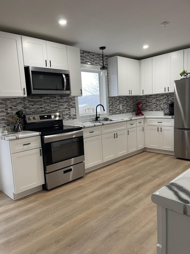 kitchen with sink, white cabinets, light hardwood / wood-style flooring, and appliances with stainless steel finishes