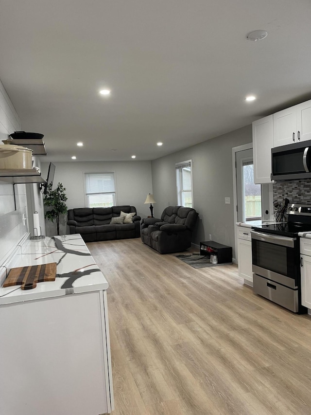 kitchen with decorative backsplash, light hardwood / wood-style floors, white cabinetry, and appliances with stainless steel finishes