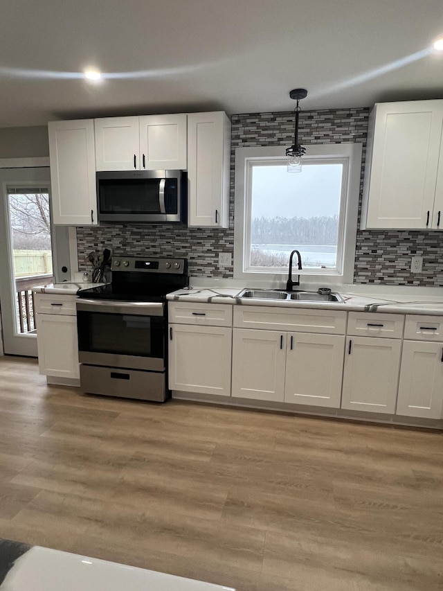 kitchen featuring pendant lighting, white cabinets, sink, appliances with stainless steel finishes, and light hardwood / wood-style floors