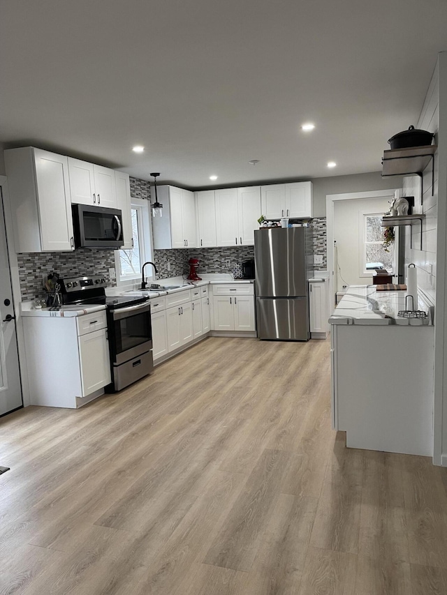 kitchen with appliances with stainless steel finishes, light wood-type flooring, backsplash, sink, and white cabinetry