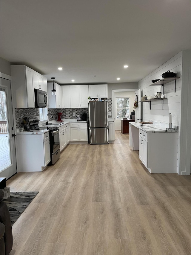 kitchen with sink, stainless steel appliances, white cabinetry, and light hardwood / wood-style flooring