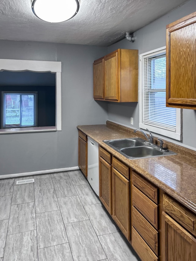 kitchen with white dishwasher, sink, and a textured ceiling