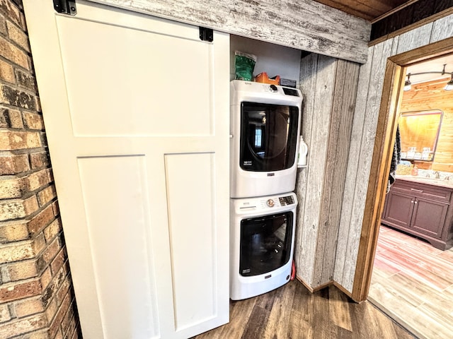 washroom with wooden walls, stacked washing maching and dryer, brick wall, and hardwood / wood-style flooring