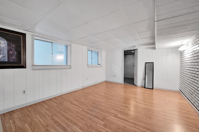 unfurnished room featuring a paneled ceiling, light hardwood / wood-style floors, and wooden walls