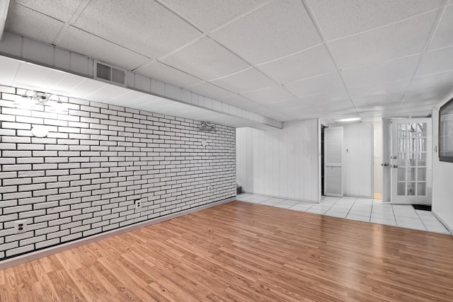 basement with a paneled ceiling, light hardwood / wood-style floors, and brick wall