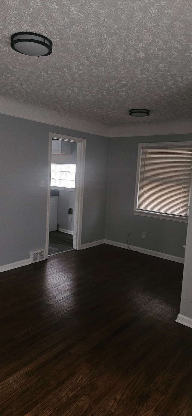 empty room with a textured ceiling and dark hardwood / wood-style floors