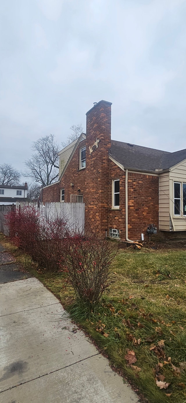 view of property exterior featuring a chimney, fence, and brick siding