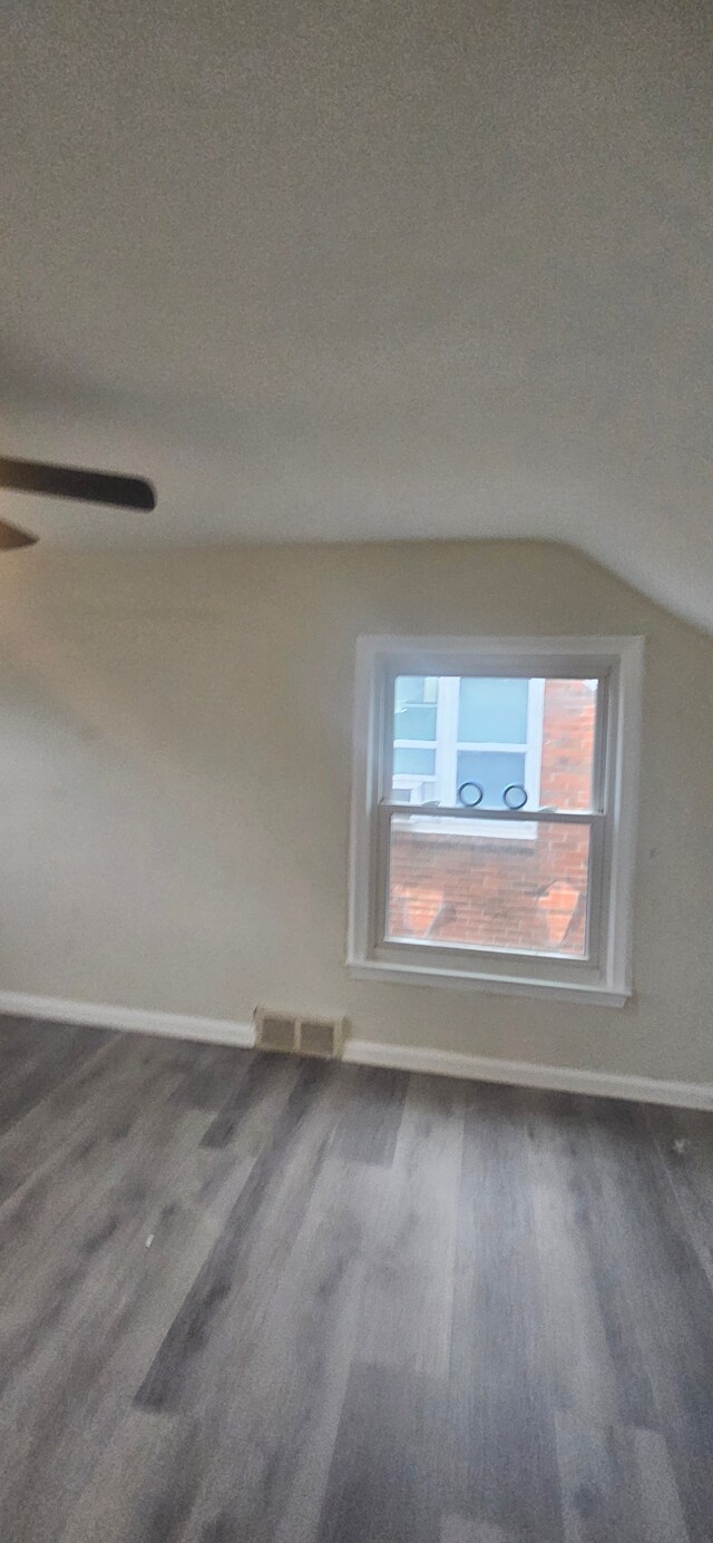 empty room with vaulted ceiling, wood finished floors, visible vents, and baseboards