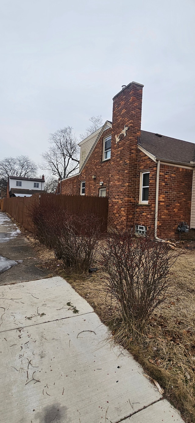 view of property exterior with brick siding, a chimney, and fence