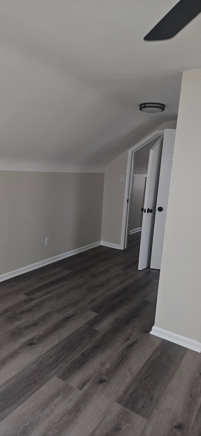 spare room with lofted ceiling, baseboards, and dark wood finished floors