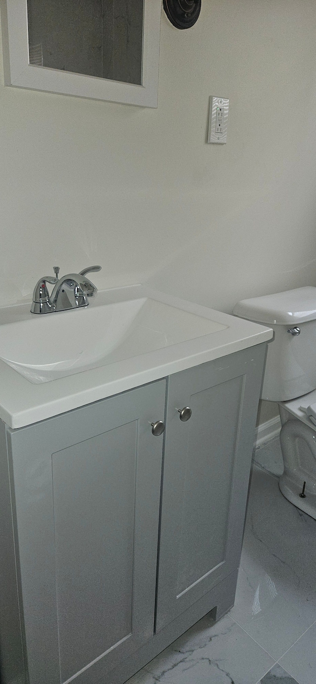 half bathroom with toilet, marble finish floor, and vanity