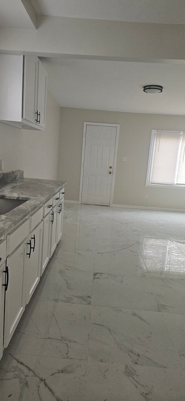 kitchen featuring a sink, white cabinetry, baseboards, marble finish floor, and light stone countertops