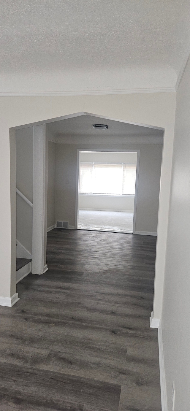 hallway with baseboards, visible vents, ornamental molding, dark wood-type flooring, and a textured ceiling