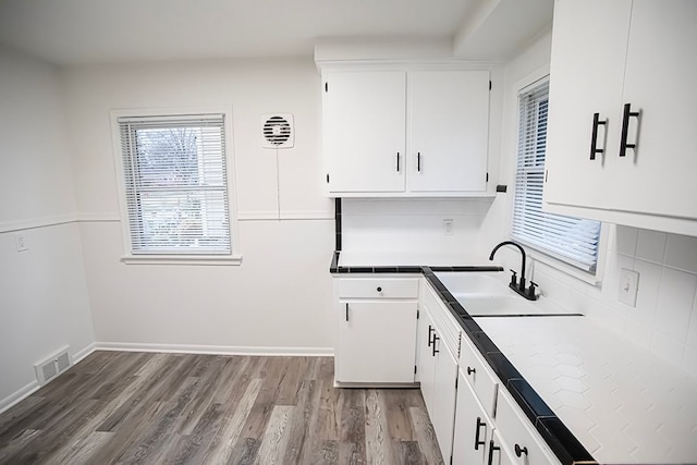 kitchen with sink, decorative backsplash, tile counters, light hardwood / wood-style floors, and white cabinetry