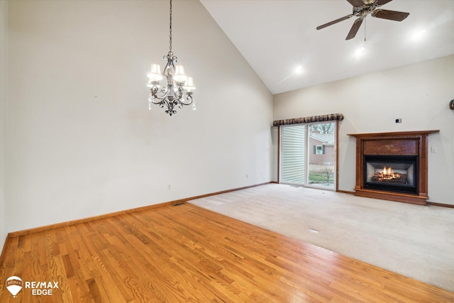 unfurnished living room featuring ceiling fan with notable chandelier, wood-type flooring, and high vaulted ceiling