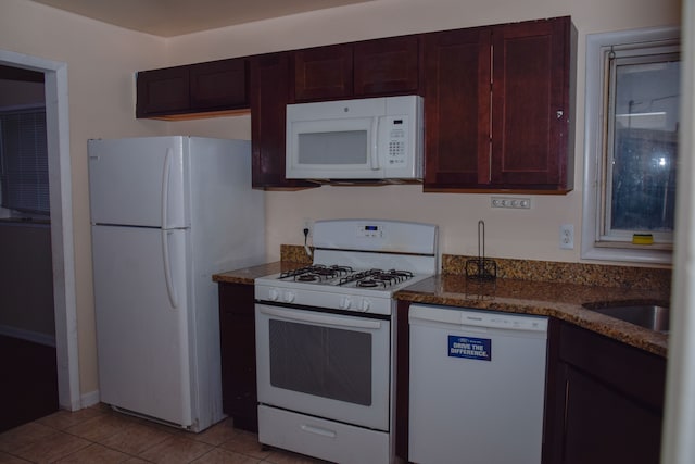 kitchen featuring white appliances, sink, light tile patterned floors, and dark stone countertops