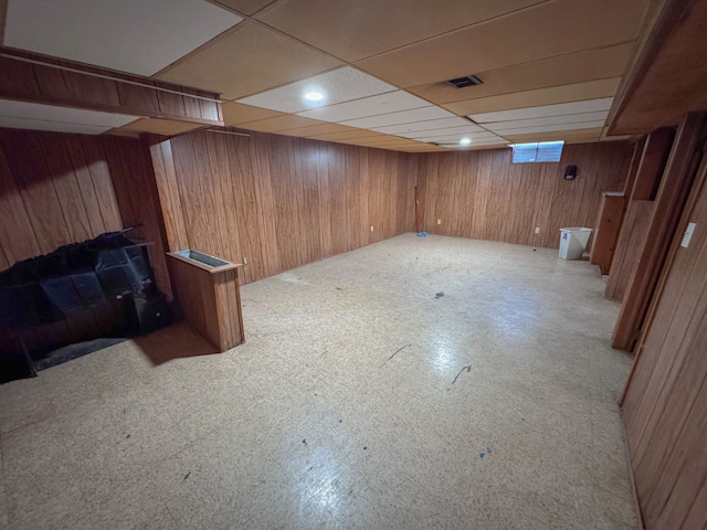 basement featuring a paneled ceiling and wood walls