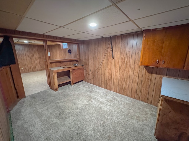 basement featuring light colored carpet, a drop ceiling, and wooden walls