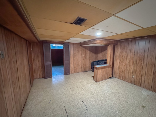 basement with wooden walls and a paneled ceiling