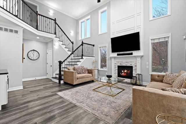 living room with a tile fireplace, dark wood-type flooring, a high ceiling, and ornamental molding