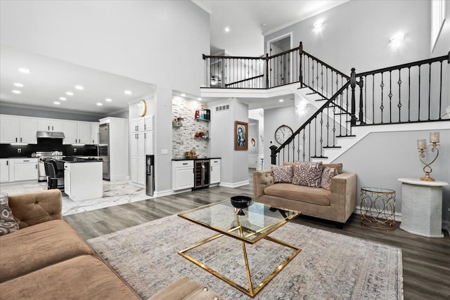 living room featuring a high ceiling, beverage cooler, crown molding, indoor bar, and hardwood / wood-style floors