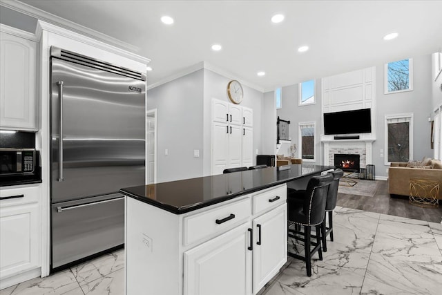 kitchen with a center island, white cabinetry, stainless steel built in fridge, and a stone fireplace