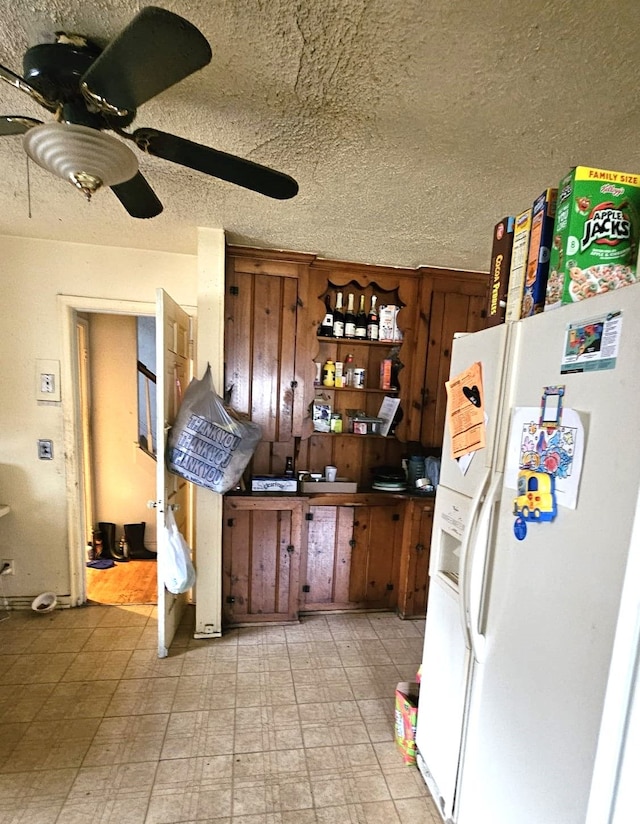 kitchen featuring ceiling fan, white fridge with ice dispenser, and a textured ceiling