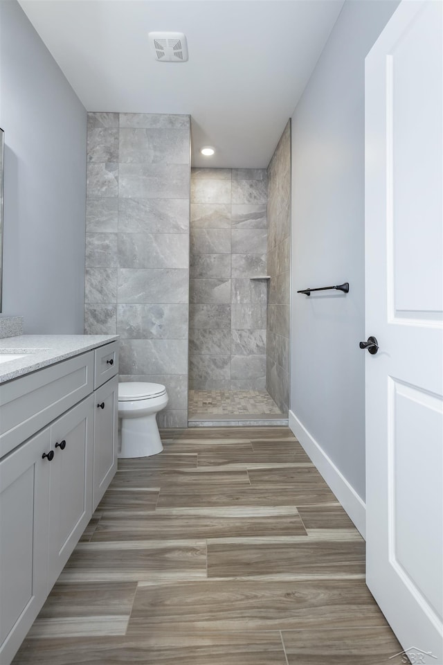 bathroom featuring a shower, vanity, toilet, and tile walls