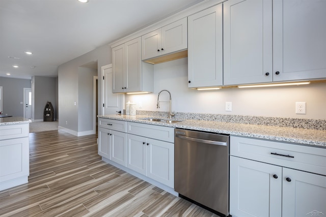 kitchen featuring dishwasher, white cabinets, sink, light hardwood / wood-style floors, and light stone counters