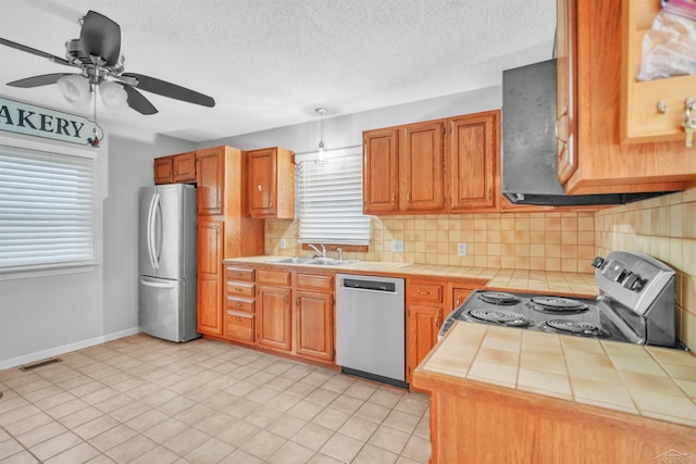 kitchen with stainless steel appliances, sink, tile countertops, ceiling fan, and plenty of natural light