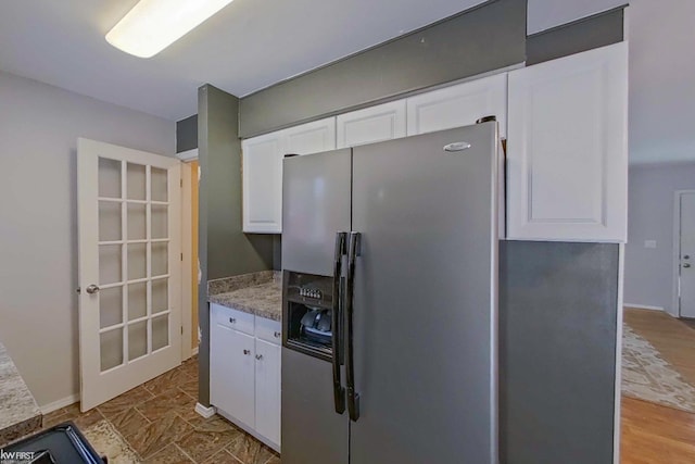 kitchen with light stone countertops, white cabinetry, stainless steel refrigerator with ice dispenser, and light wood-type flooring