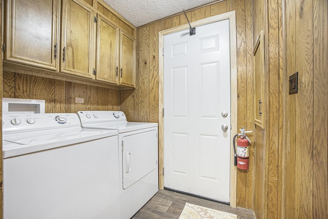 laundry room featuring cabinets, dark hardwood / wood-style flooring, a textured ceiling, wooden walls, and independent washer and dryer