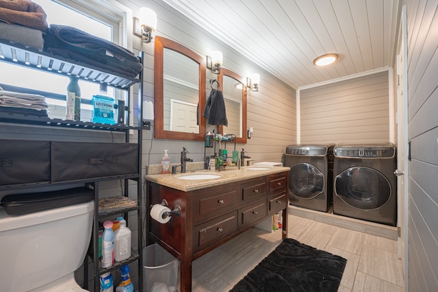 bathroom featuring washing machine and dryer, wood walls, vanity, and toilet