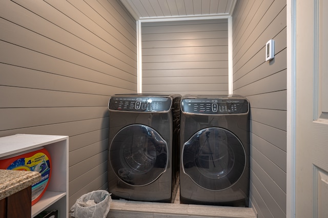 clothes washing area featuring washer and clothes dryer and wooden walls