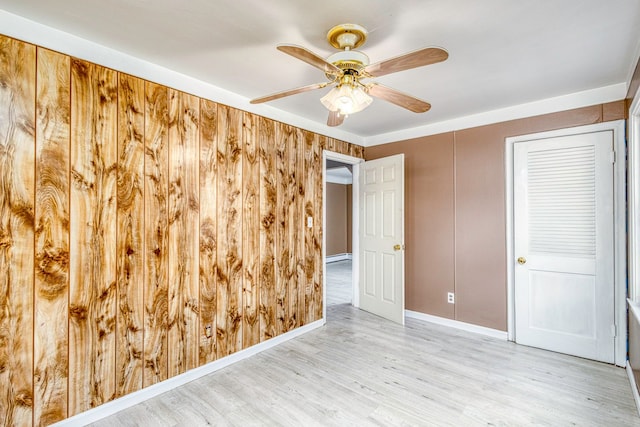 spare room featuring baseboard heating, wood walls, ceiling fan, and light wood-type flooring