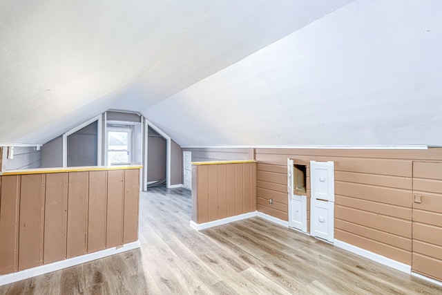 bonus room featuring lofted ceiling, wooden walls, and light hardwood / wood-style flooring